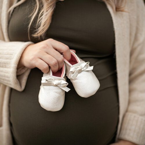 a pregnant woman holding a pair of baby shoes